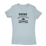 Image of a Light Blue t-shirt with a white text graphic that reads 'NEVER UNDERESTIMATE THE POWER' with a crown symbol above the text, promoting a message of empowerment and resilience.