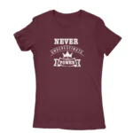 Image of a Maroon t-shirt with a white text graphic that reads 'NEVER UNDERESTIMATE THE POWER' with a crown symbol above the text, promoting a message of empowerment and resilience.