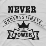 close up image of Empowerment Tee by Apparel by Cetakshop. T Shirt for women decorated with  print of 'NEVER UNDERESTIMATE THE POWER' with a crown symbol above the text, promoting a message of empowerment and resilience.